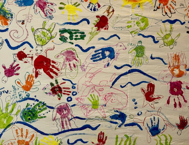 Auf einem Wandbild sind farbige Handabdrücke, Linien und Kleckse zu sehen.