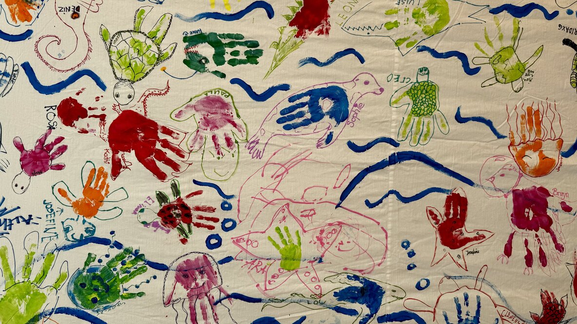 Auf einem Wandbild sind farbige Handabdrücke, Linien und Kleckse zu sehen.