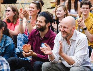 Humanistische Fachschule für Sozialpädagogik in Berlin: Rückblick Studierende der Humanistischen Fachschule für Sozialpädagogik sitzen in mehreren Reihen im Freien und klatschen.