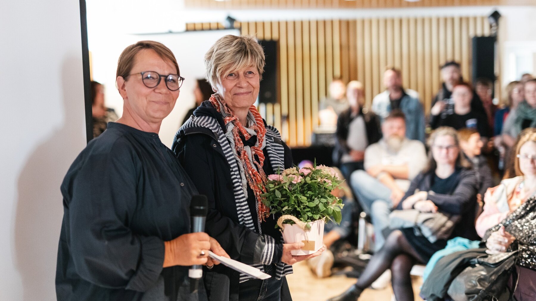 Britta Licht, Abteilungsleitung Humanistische Kindertagesstätten im Humanistischen Verband Berlin-Brandenburg, steht neben einer Frau mit Rosenpflanze im Blumentopf in den Händen.