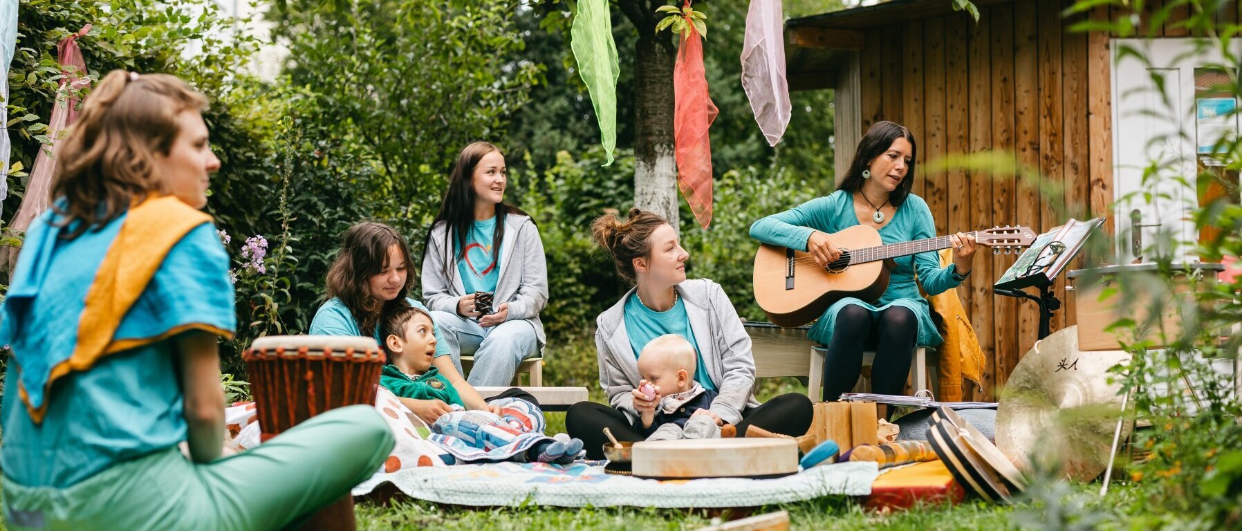 Mehrere Menschen sitzen im Garten. Sie machen gemeinsam Musik und lachen.