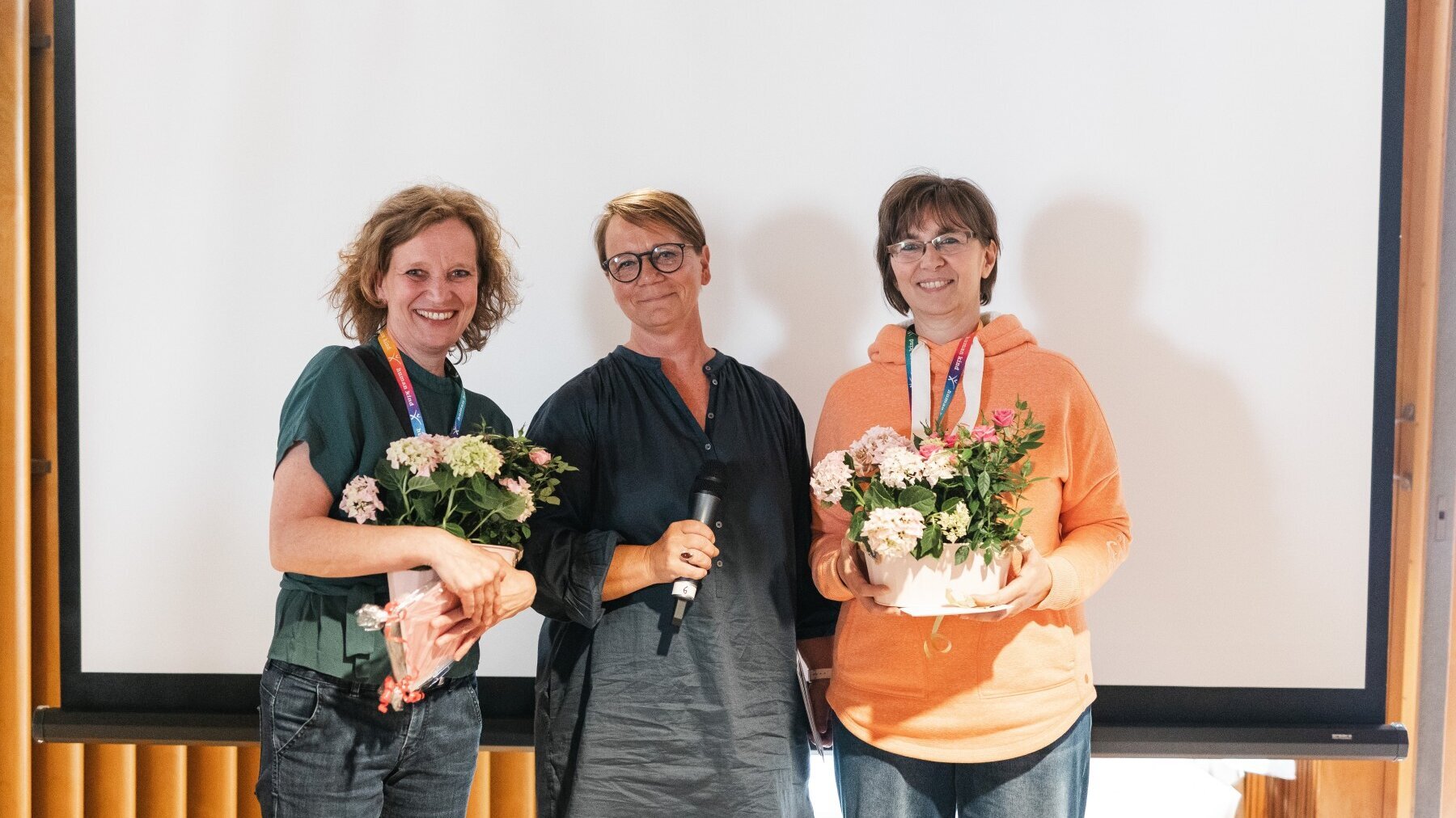 Britta Licht, Abteilungsleitung Humanistische Kindertagesstätten im Humanistischen Verband Berlin-Brandenburg, steht in der Mitte neben zwei Frauen mit Rosenpflanze im Blumentopf in den Händen.
