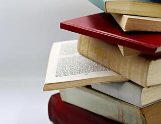 Humanistische Akademie Berlin-Brandenburg: Humanismusforschung und Humanistik Rechts ist ein Stapel Bücher zu sehen, die nicht ordentlich Kante auf Kante übereinanderliegen.