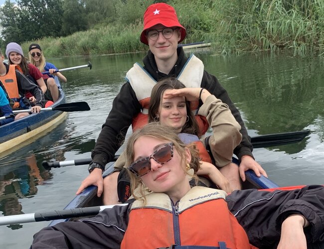Drei Jugendliche sitzen hintereinander in einem Kanu im Wasser.