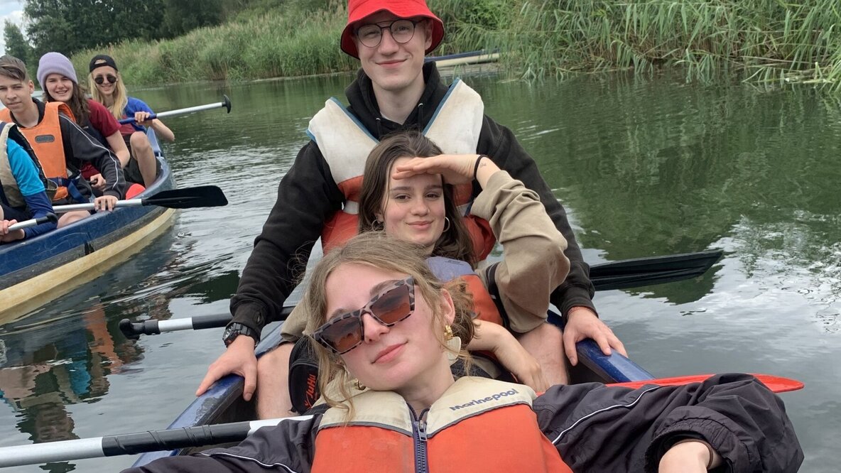 Drei Jugendliche sitzen hintereinander in einem Kanu im Wasser.