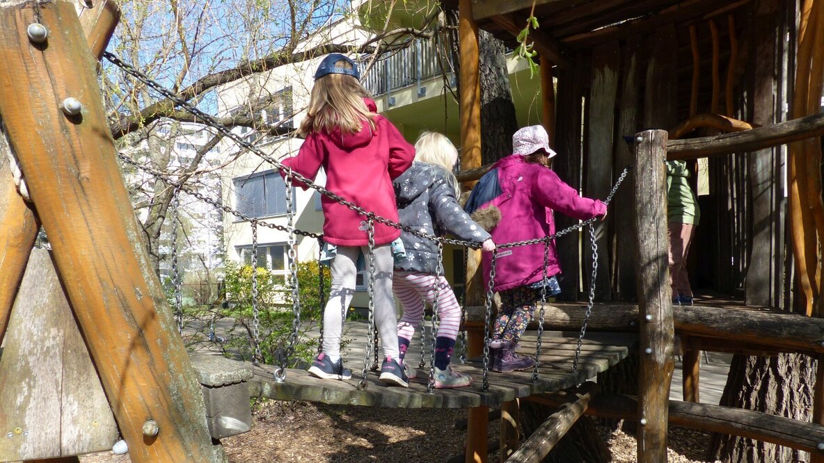 Drei Mädchen laufen über eine Hängebrücke im Kitagarten.