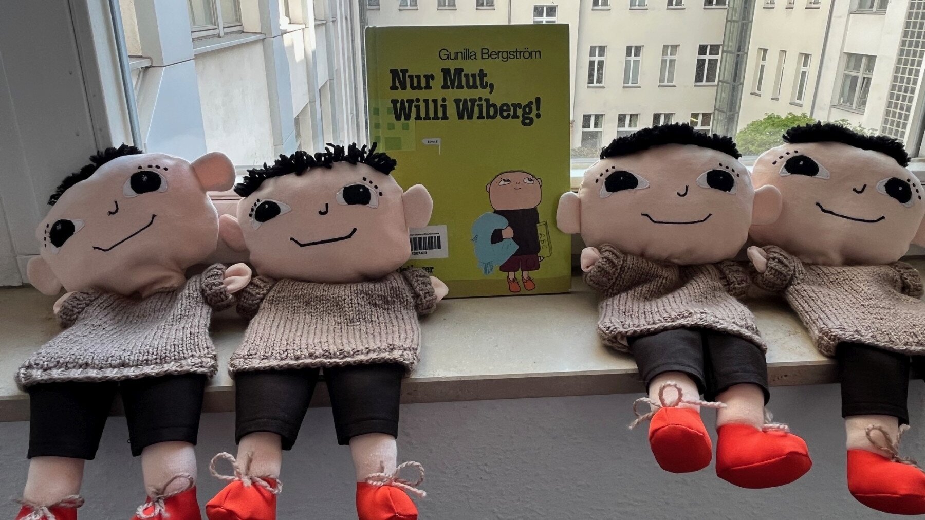 Auf einem Fensterbrett liegen vier Willi-Wiberg-Handpuppen. In der Mitte lehnt am Fenster das Buch „Nur Mut, Willi Wiberg!“ von Gunila Bergström.