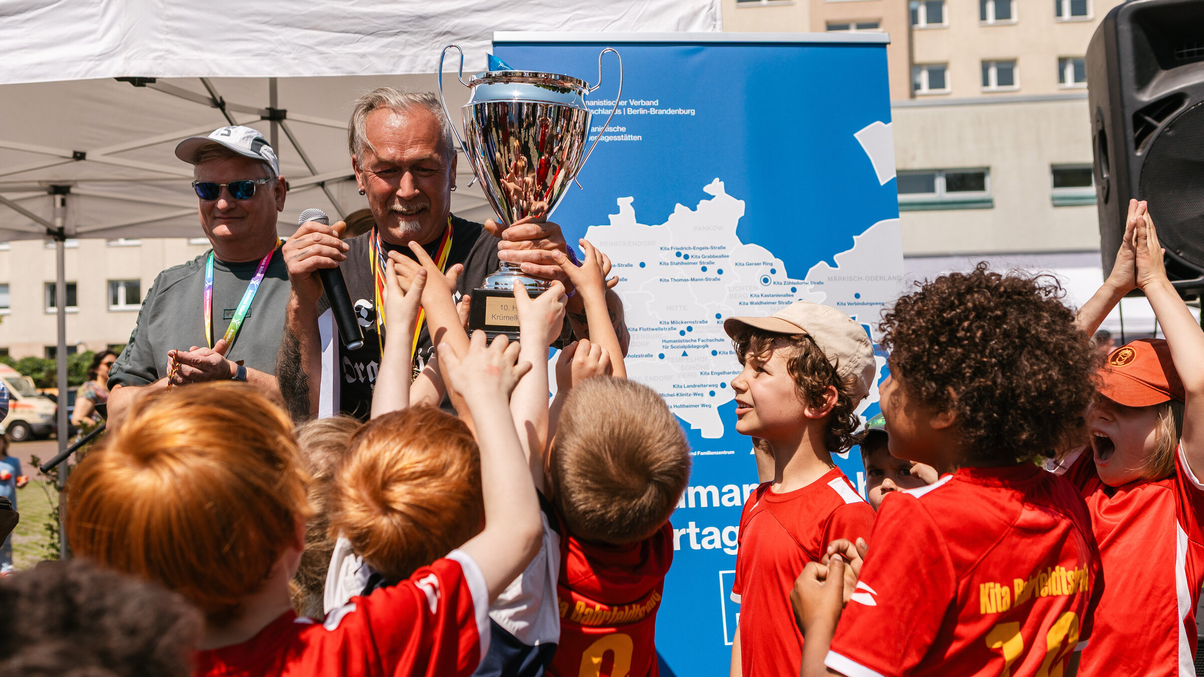 Ein kleine Gruppe Kinder halten gemeinsam einen großen Pokal in die Höhe, der ihnen eben überreicht wurde.