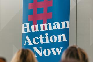 Human Action Now: Engagieren im Humanistischen Verband Berlin-Brandenburg Auf einem Roll-up des Humanistischen Verbandes Berlin-Brandenburg steht auf Blau nach einem roten Hashtag Folgendes in Weiß: „Human Action Now“.