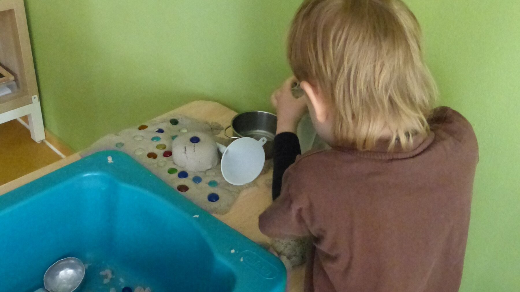 Ein Junge steht an einem Tisch mit eingelassener Plastikwanne und experimentiert.