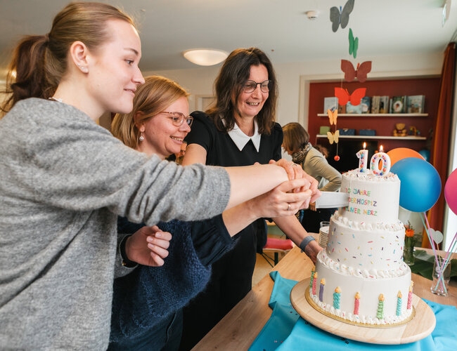 Drei Personen schneiden gemeinsam eine Torte an, die auf einem Tisch steht.