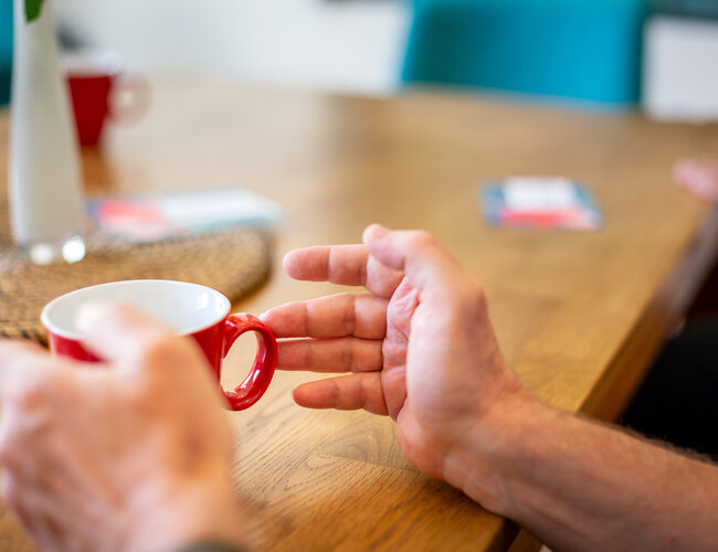 Hände halten eine auf einem Tisch stehende Tasse.