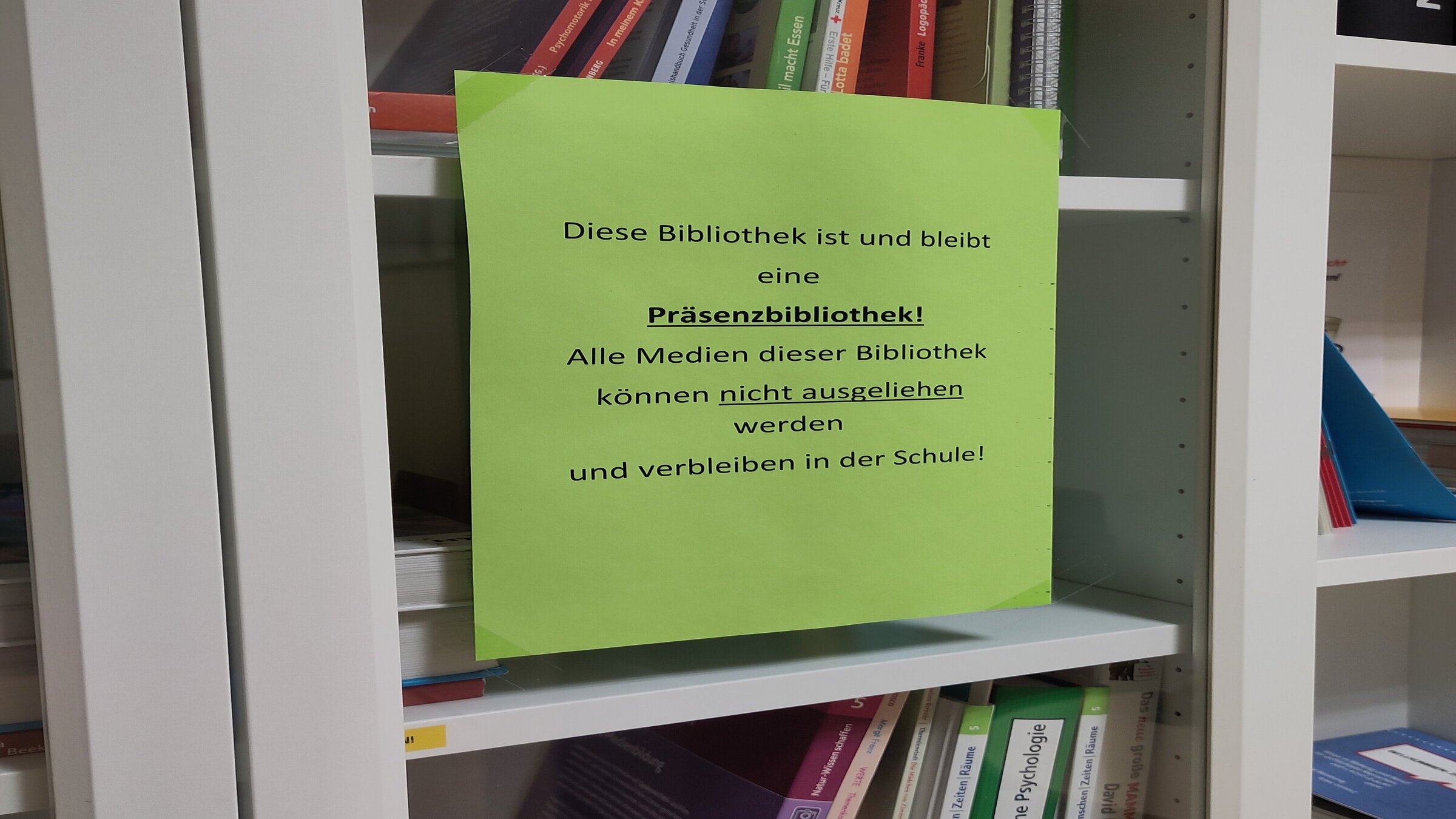 Bücherschrank in Präsenzbibliothek mit Aushang