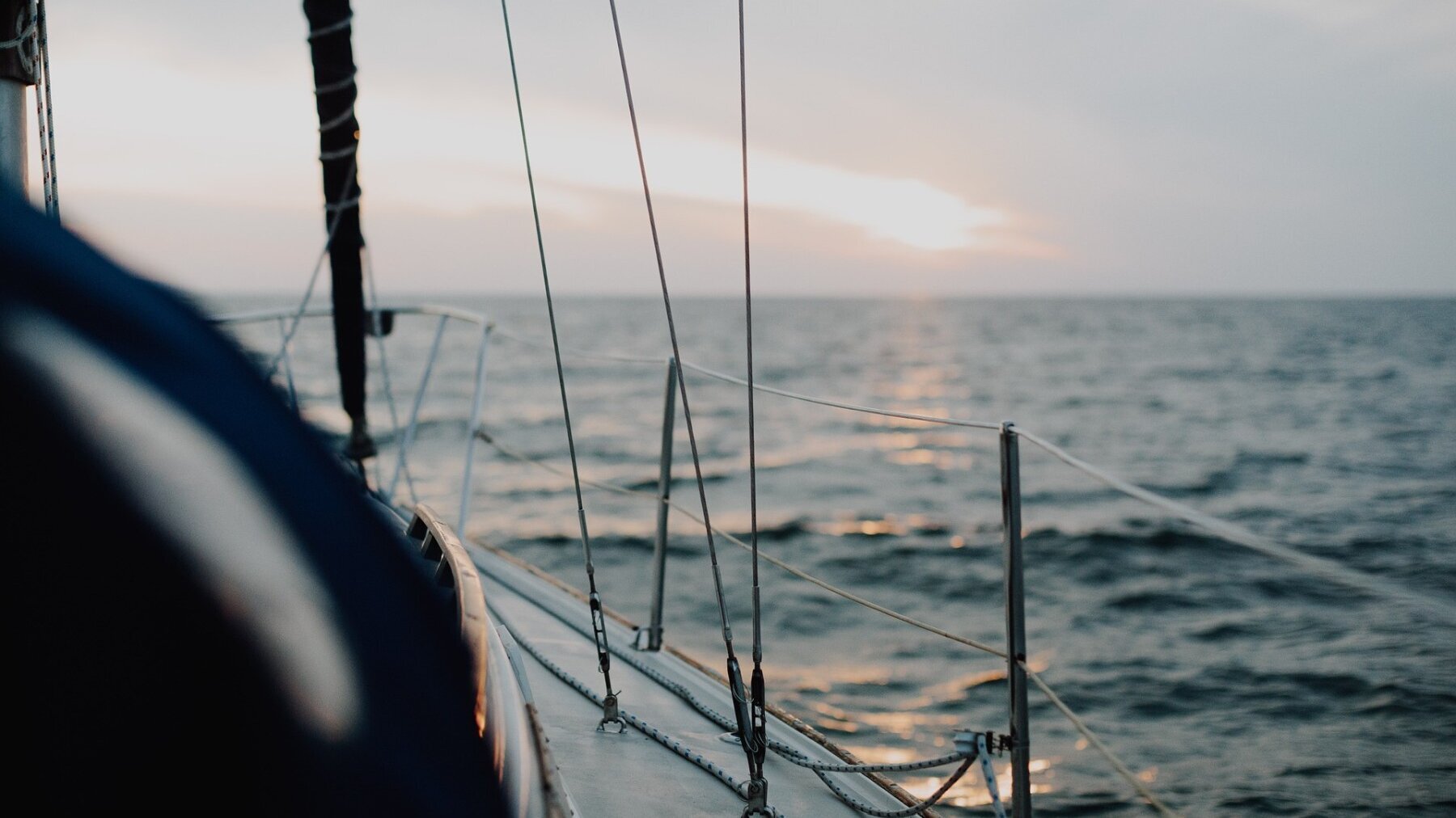 Links im Bild ist der rechte vordere Bereich einer Segeljacht und rechts sowie hinten sind ein Gewässer und der Horizont zu sehen.