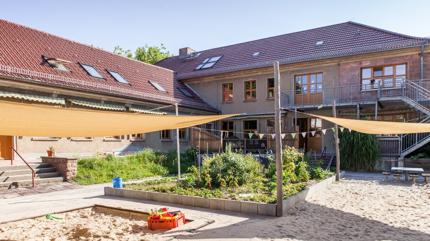 Foto Außenansicht Spielplatz Kita Friedrich-Engels-Straße mit Sandkasten und Beet