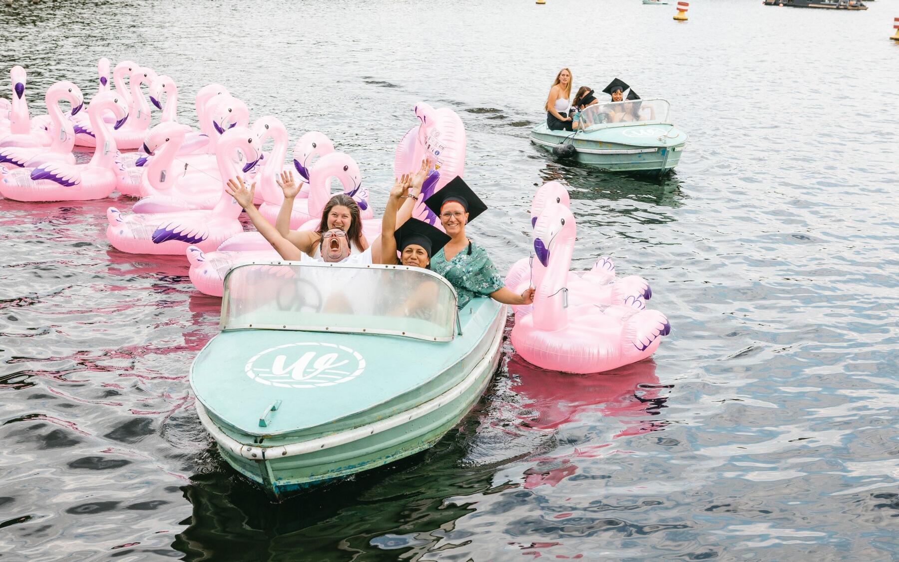 Zwei Tretboote mit jeweils mehreren Personen an Bord sind auf dem Wasser zu sehen. Dazwischen schwimmen aufblasbare Flamingos.
