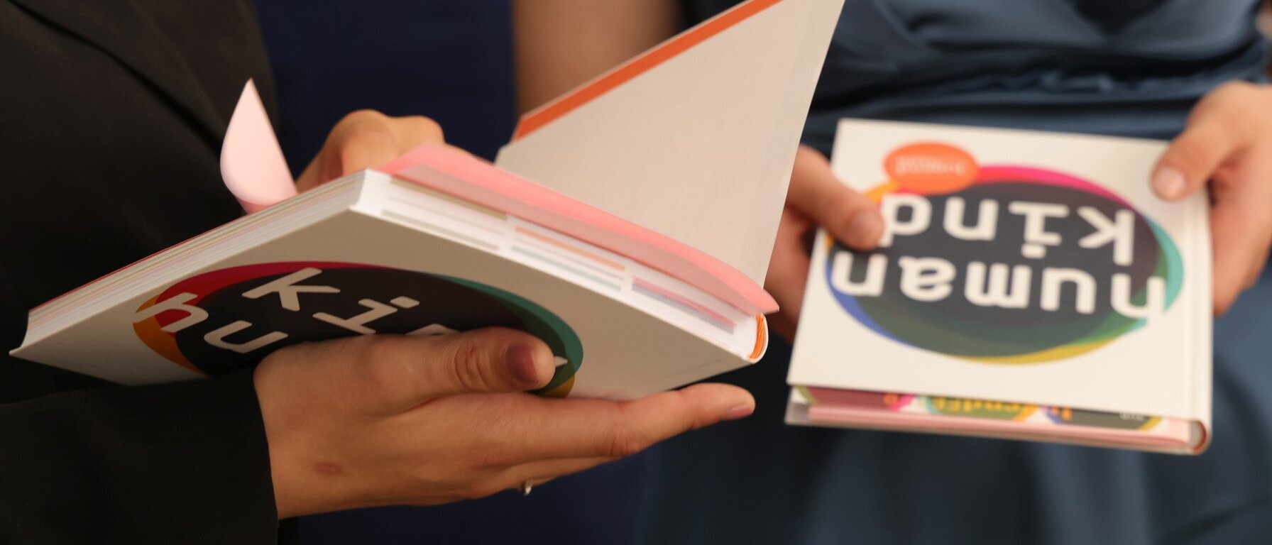 Auf einer Tischplatte liegen in zwei Stapeln nebeneinander Expemplare des Buchs „Human Kind – Kind Human“ für Jugendliche, die an einer JugendFEIER des Humanistischen Verbandes Berlin-Brandenburg teilnehmen.