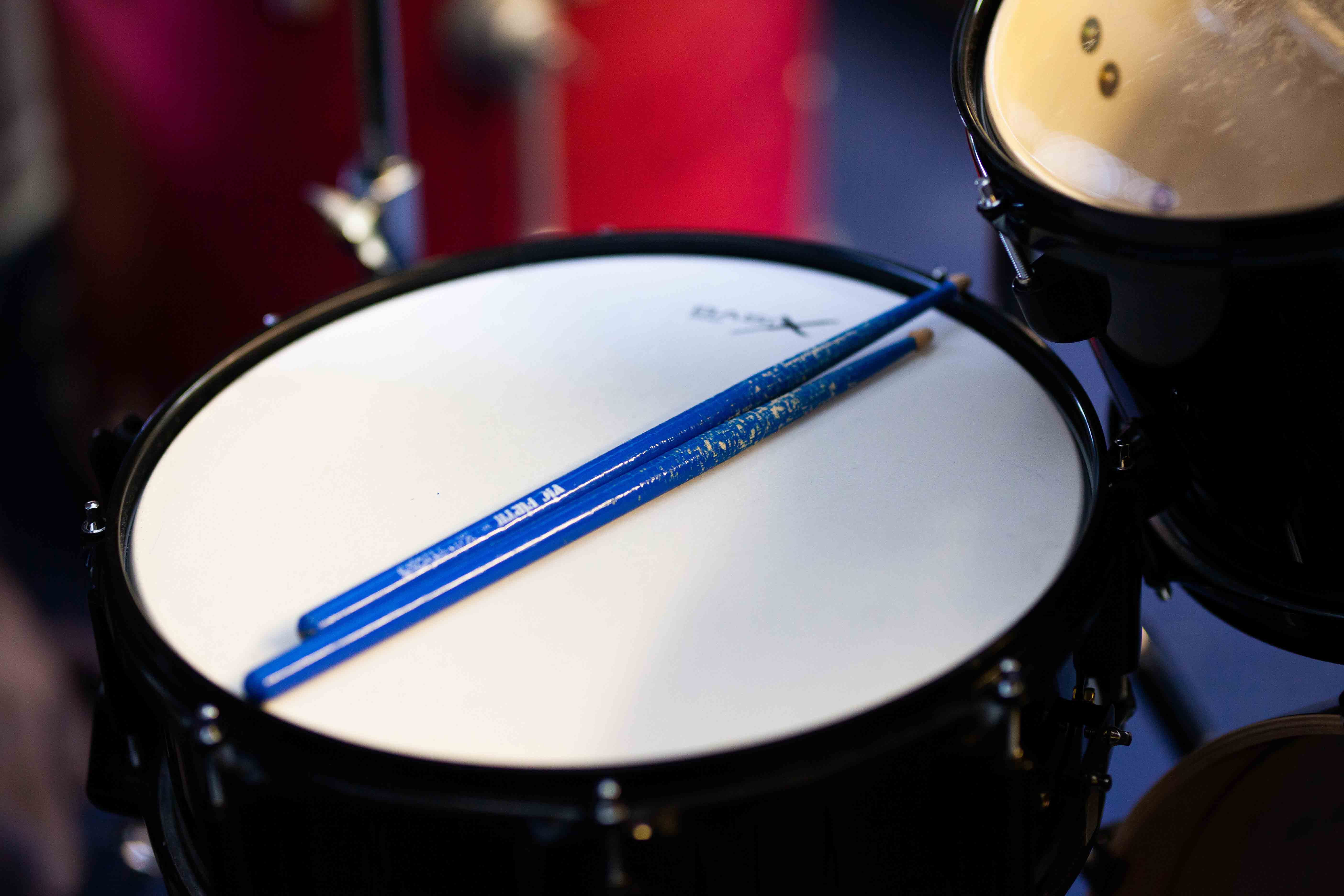 Man sieht zwei Trommelsticks nebeneinander auf einer blauen Trommel liegen.