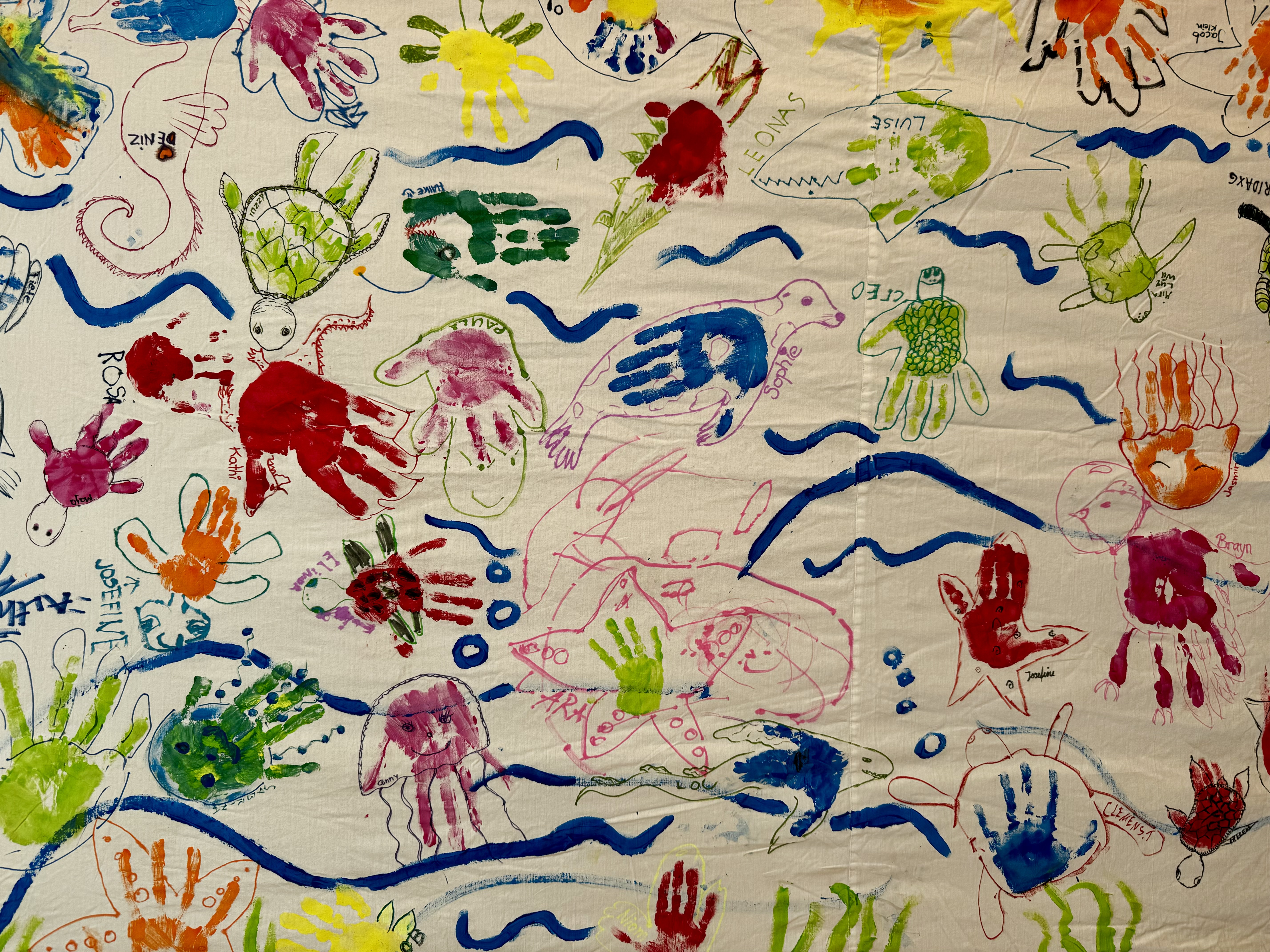 Auf einem Wandbild sind farbige Handabdrücke, Linien und Kleckse zu sehen.