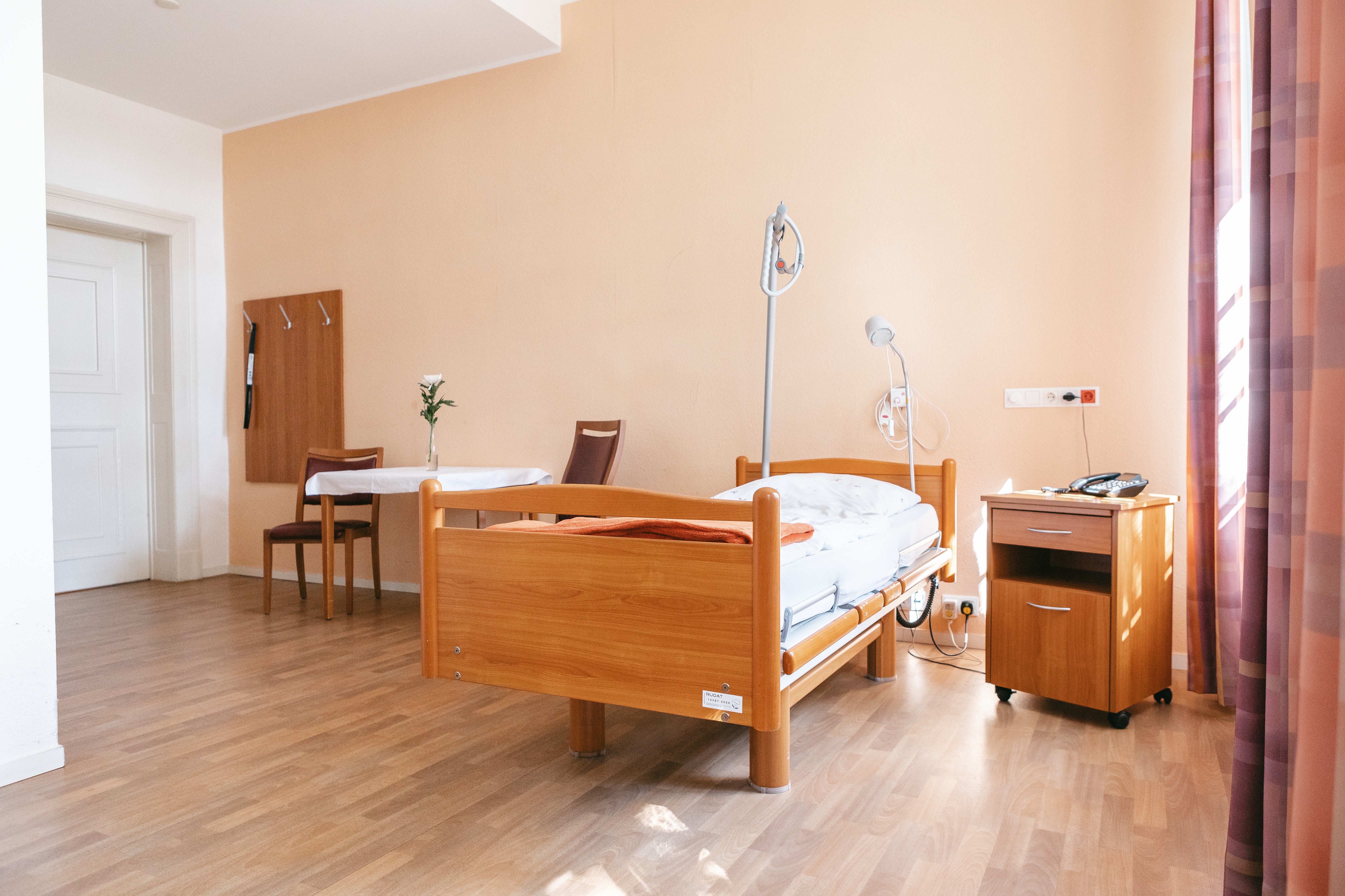 Zu sehen ist ein großer heller Raum. In der Mitte an der Wand steht ein Bett daneben Nachttische.