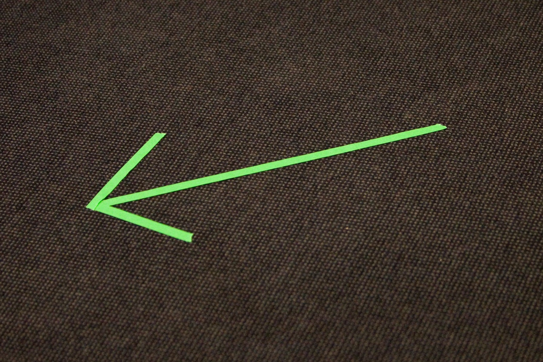 Auf einem schwarzen Teppich ist ein Pfeil aus neongrünen Klebestreifen zu sehen, der nach rechts zeigt.