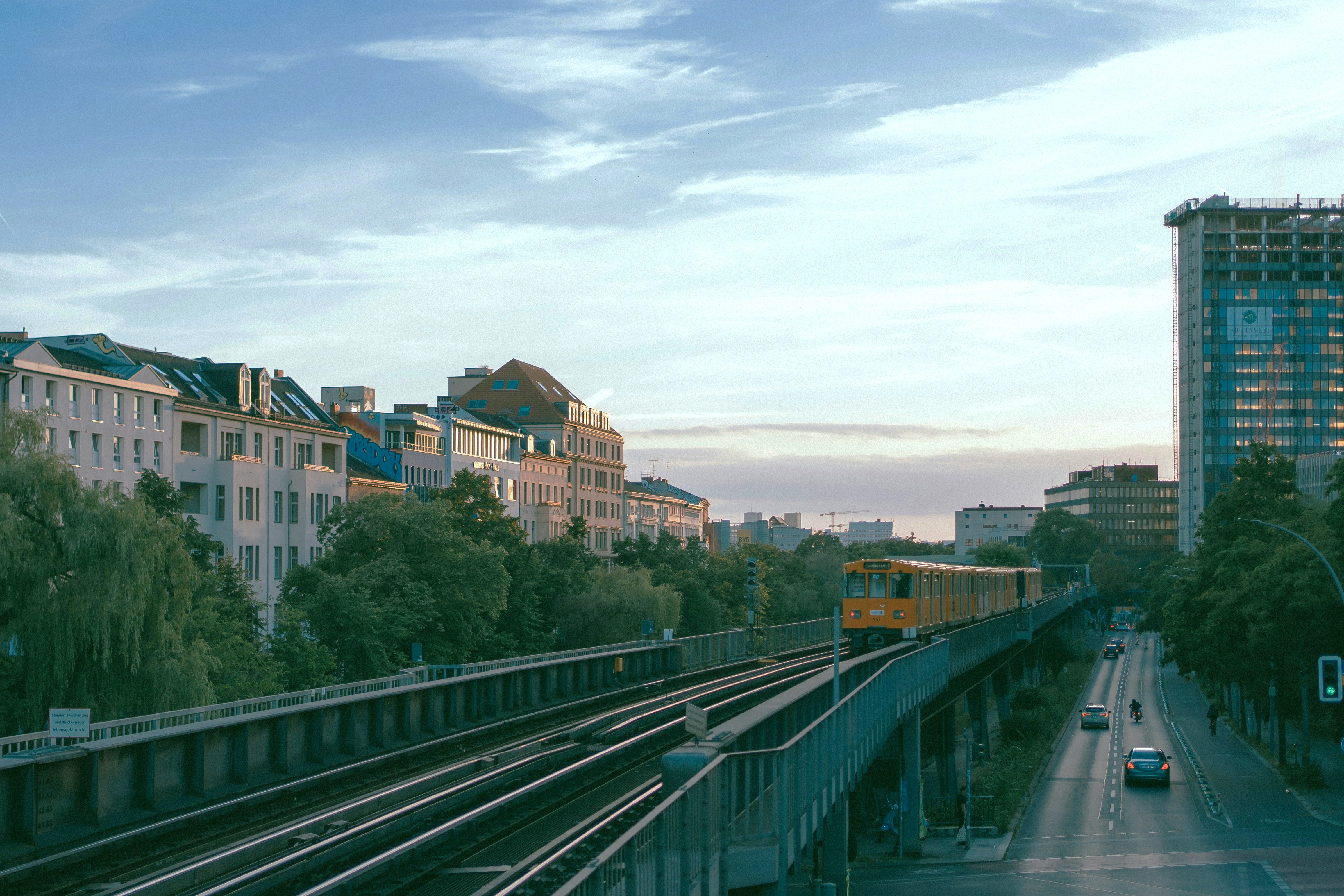 Zu sehen ist eine Berliner U-Bahn, die neben hohen Gebäuden auf Bahngleisen fährt.