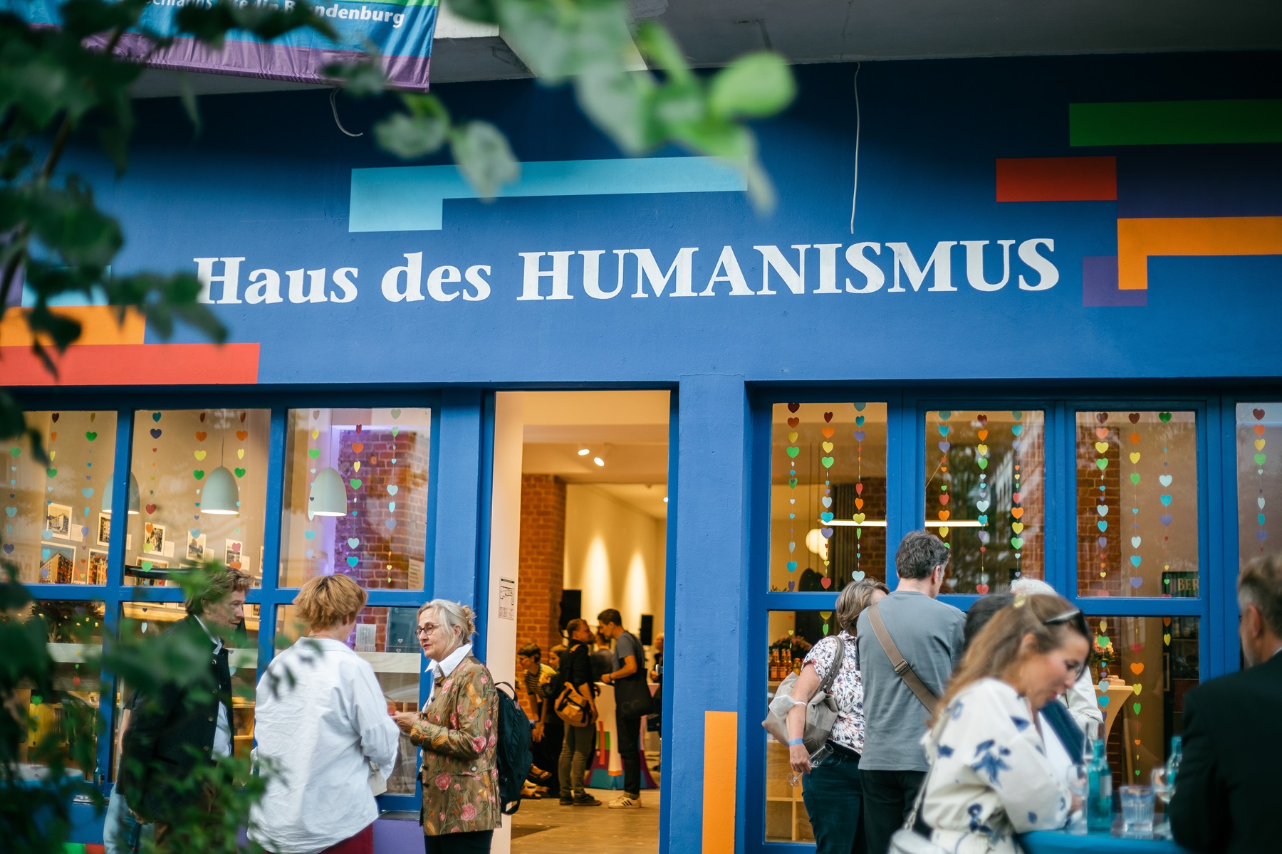 Menschen stehen in feierliche Stimmung vor und in einem Veranstaltungsort mit blauer Fassade und Schriftzug: Haus des HUMANISMUS