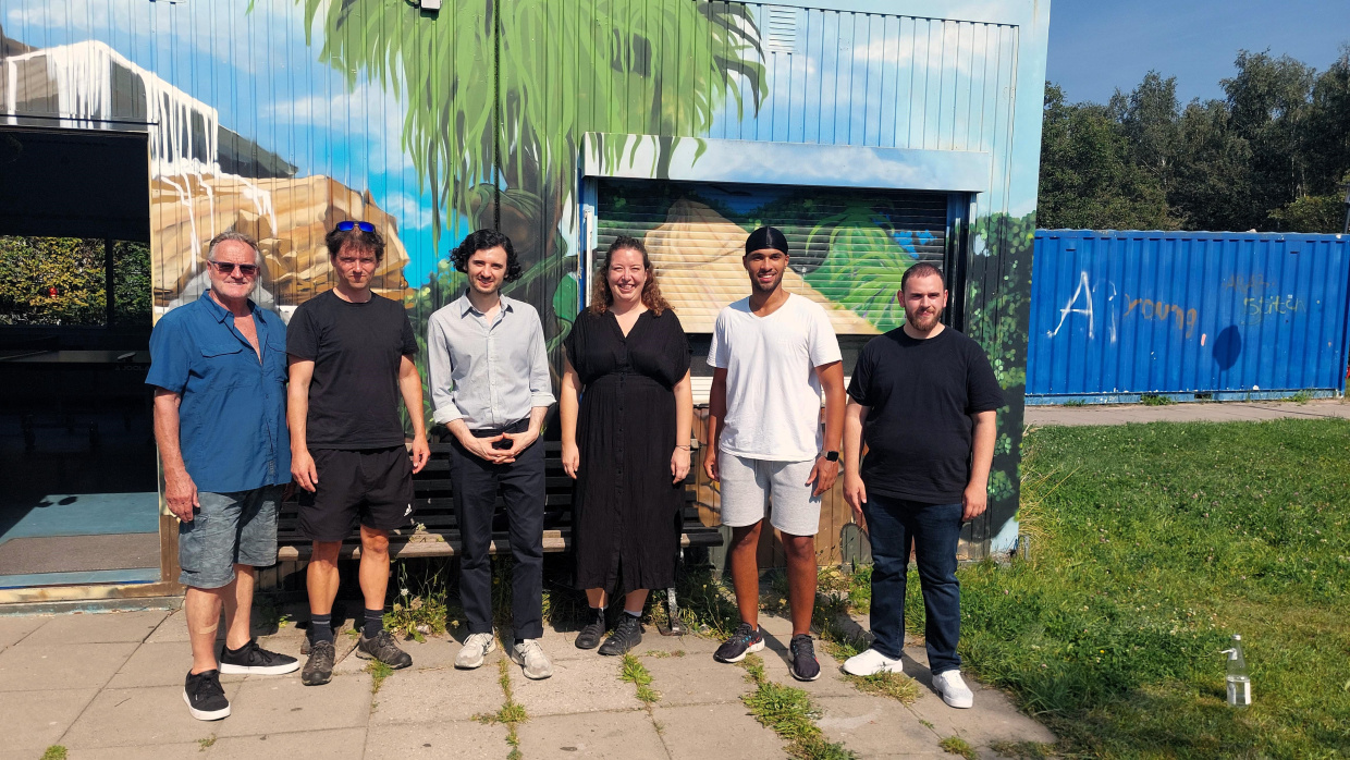 Sechs Personen stehen vor dem Container der Jugendfreizeiteinrichtung BlueBox des Humanistischen Verbandes Berlin-Brandenburg, darunter Dr. Bruno Osuch, Verantwortlicher für die politische Kommunikation im Verband, Einrichtungsleitung Fabian Rohmer, Bundestagsabgeordneter Hakan Demir und Dorina Thomas, stellvertretende Leitung der Abteilung Jugend im Verband.