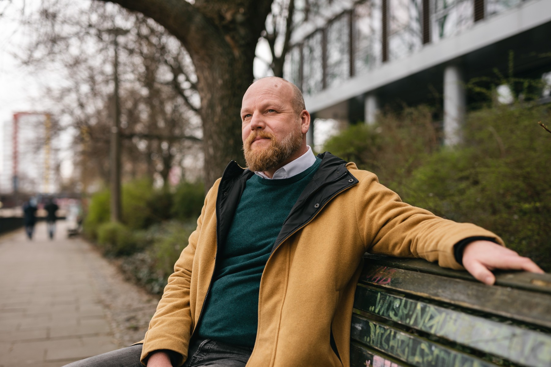 Matthias Krahe, Abteilungsleiter Humanistische Lebenskunde im Humanistischen Verband Berlin-Brandenburg, sitze auf einer Bank, wobei sein linker Arm oben auf der Lehne ruht.